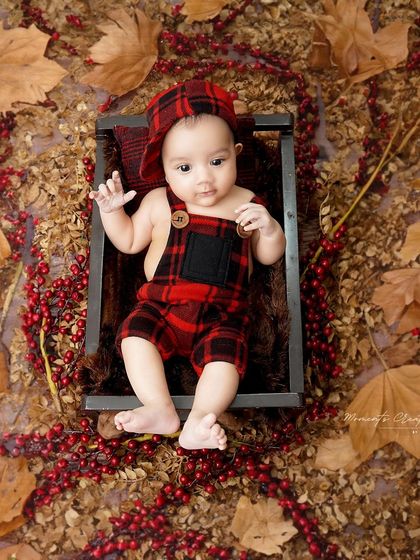 An autumn-themed flat lay for a three-month-old. Dressed in plaid overalls, this little one is surrounded by fall leaves and berries, creating a warm and rustic portrait.