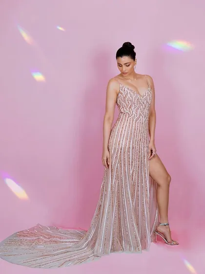 A graceful shot of Daisy Shah looking down, highlighting the delicate straps and intricate beadwork of her gown. The pose conveys a sense of quiet elegance.