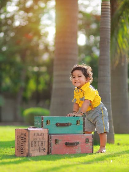 Using vintage props like these colorful trunks adds a touch of charm to outdoor kids' photoshoots. This little boy is all smiles during his sunny park session.