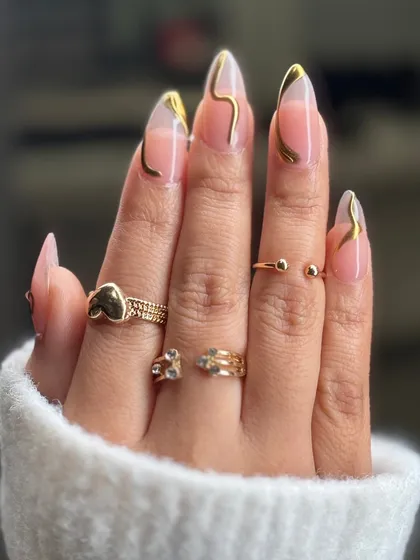 Abstract sculpted gold art on long, clear extensions. The flowing gold lines create a sense of movement and luxury, making for a sophisticated and modern manicure.