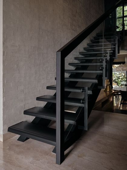 We designed this modern, minimalist staircase with black metal and glass. It acts as a sculptural element against the textured concrete wall, embodying a raw yet refined aesthetic.