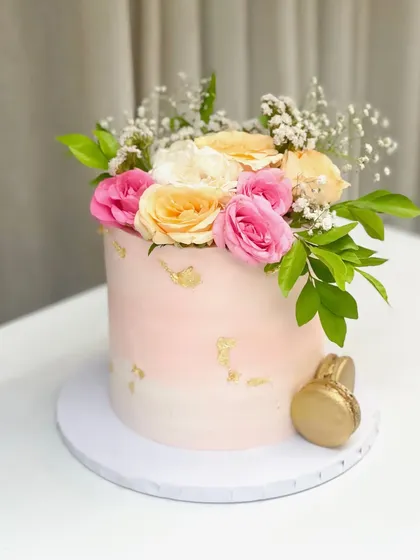 A fresh and vibrant cake for a 50th birthday. This double barrel vanilla cake with mango and cream filling is decorated with an ombre pink finish, gold leaf, and a crown of fresh roses.
