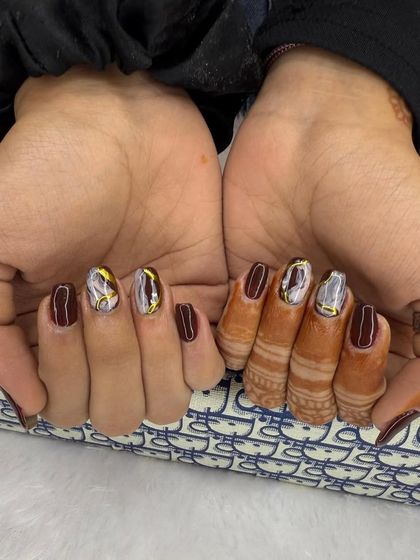 A chic and edgy design on short nails. This set combines a deep maroon polish with accent nails featuring a shattered glass effect in silver and gold.