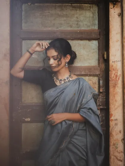 A full-length portrait against a rustic, weathered door. The model's relaxed, leaning pose and the earthy tones of the background create a grounded and soulful image.