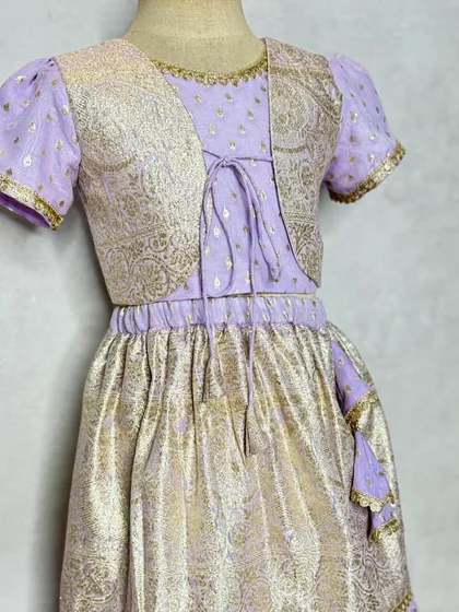 This lavender and gold lehenga set includes a short, embroidered jacket for a layered look. The metallic brocade fabric gives it a festive shimmer.