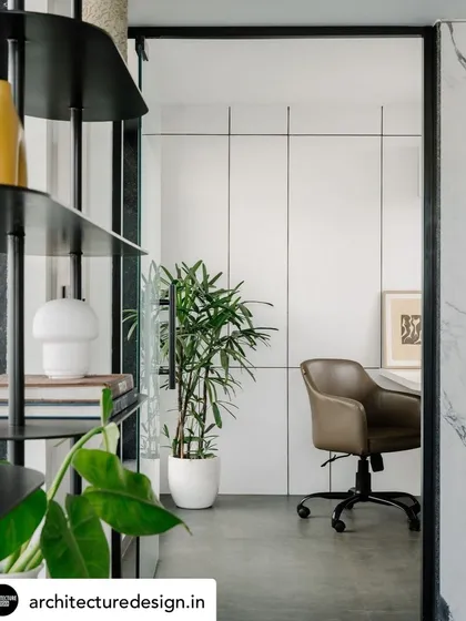 A view into a private office, framed by a black metal shelving unit, demonstrating the use of partitions to create distinct zones while maintaining a sense of openness.