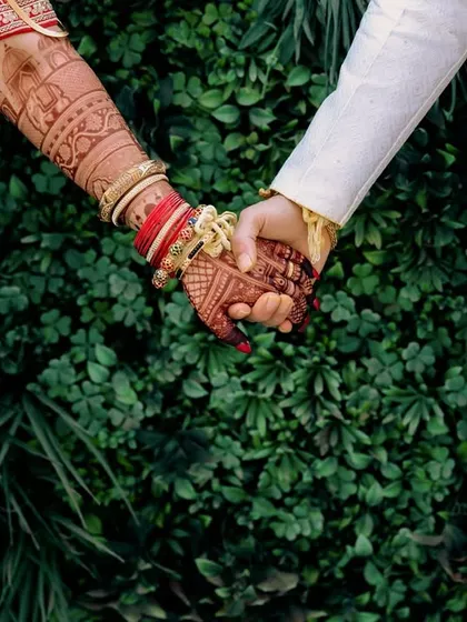 A close-up of the couple's hands, showcasing the bride's intricate henna and traditional red bangles. This detail shot symbolizes the joining of two lives in a Marathi wedding.