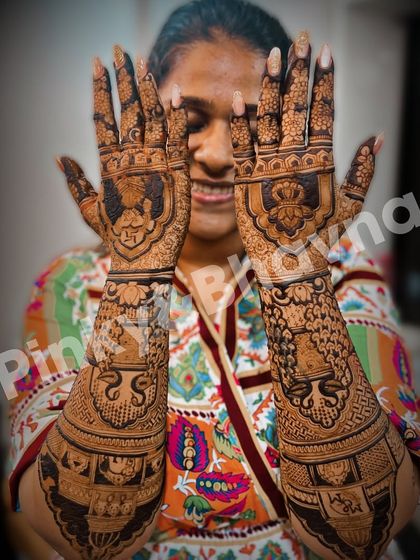 A happy bride showing her full bridal mehndi. The design is a beautiful mix of portraits, figures, and traditional patterns.