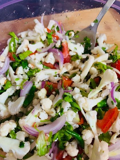 A fresh cauliflower salad with onions, tomatoes, and herbs.