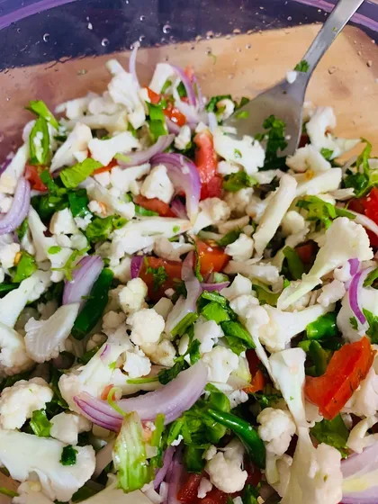 A fresh cauliflower salad with onions, tomatoes, and herbs.