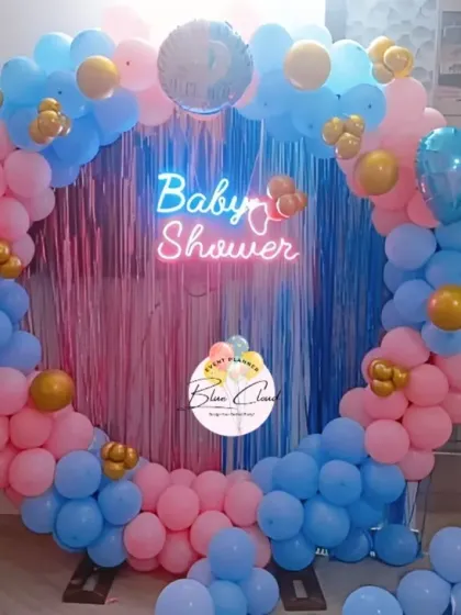 A classic gender reveal baby shower with a pink and blue balloon ring, shimmer curtain, and neon sign.