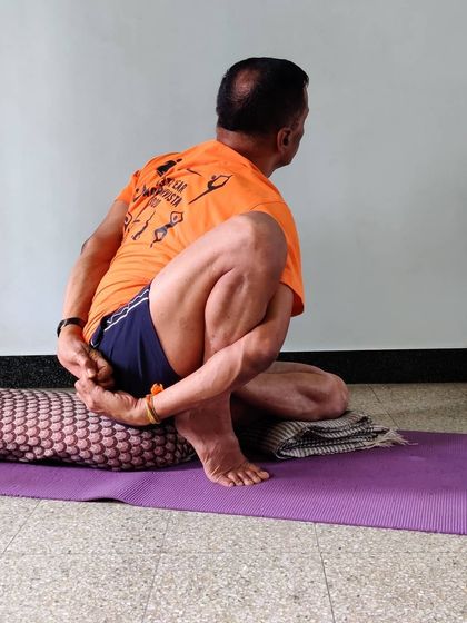 Marichasana 2 involves a half-lotus position, which deepens the stretch in the hips and back. Notice how the bolster provides support to maintain the posture correctly.