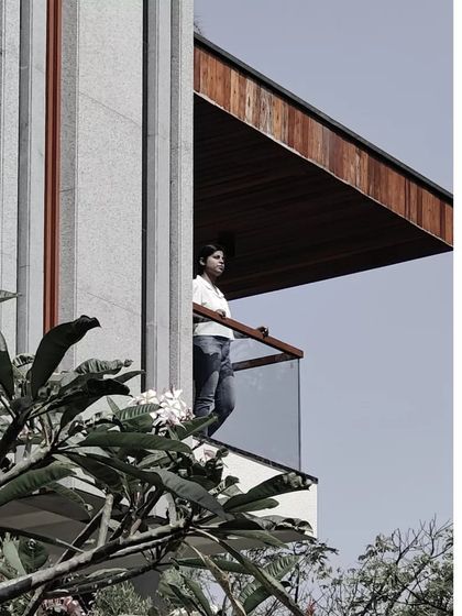 A detail of the Janani House, where a resident enjoys the view from a cantilevered balcony. The design provides private outdoor spaces for each level, connecting the inhabitants to their surroundings while maintaining a sense of enclosure.