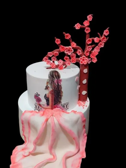 A beautiful cake featuring a hand-painted girl in a flowing pink dress, sitting beside an edible cherry blossom tree. This design is both artistic and elegant.