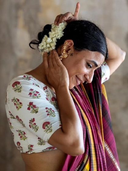 A model adjusts jasmine in her hair, wearing a beautiful hand-block printed sari blouse, part of a new collection launching at our festival.