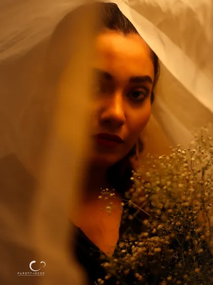 A dreamy and ethereal portrait, shot through a sheer white veil. The soft, golden light and the baby's breath flowers create a romantic and delicate mood.