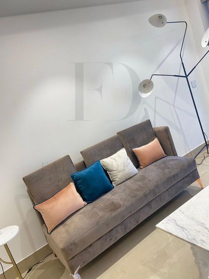 A comfortable sofa-bed in a neutral brown fabric, perfect for a multifunctional space. It's paired with colorful cushions and a modern floor lamp with an integrated marble side table for added utility.