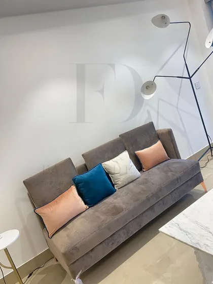 A comfortable sofa-bed in a neutral brown fabric, perfect for a multifunctional space. It's paired with colorful cushions and a modern floor lamp with an integrated marble side table for added utility.
