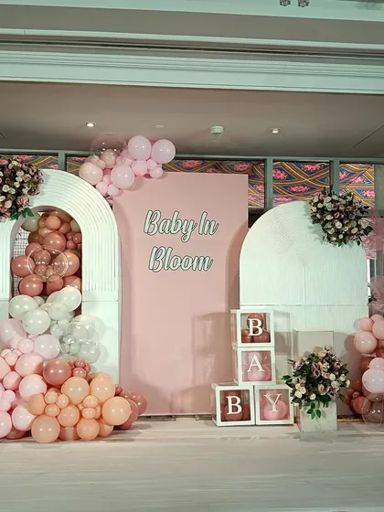 A lovely "Baby in Bloom" theme with a soft pink color palette. The setup includes arched backdrops, floral accents, and "BABY" blocks for a classic baby shower look.