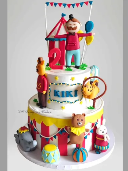 A festive two-tier carnival theme cake for a 2nd birthday. This detailed cake includes a ringmaster, circus animals, and a big top tent design.