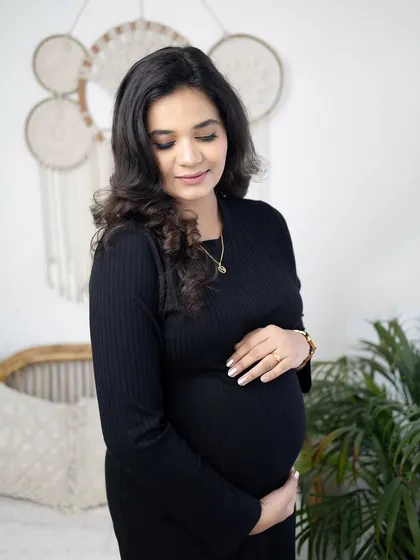 A quiet, reflective solo portrait of the mother-to-be cradling her bump. The indoor setting with natural light provides a soft and gentle atmosphere.