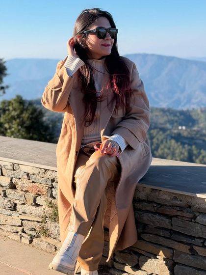 Enjoying the mountain view in a beige monochromatic outfit. A long trench coat paired with matching trousers and white boots is a stylish choice for a winter trip.