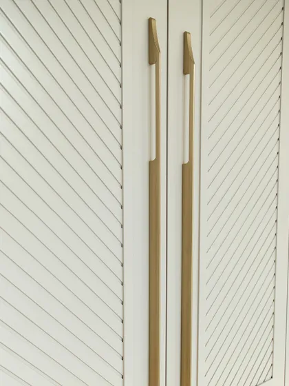 A close-up of the elegant, elongated handles against the chevron-patterned wardrobe shutters, showcasing our attention to high-quality hardware.