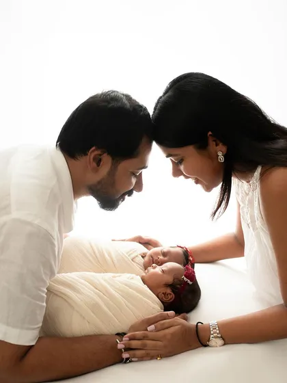 A beautiful family portrait with newborn twins. The parents are looking at each other, sharing a moment of pure joy and love.