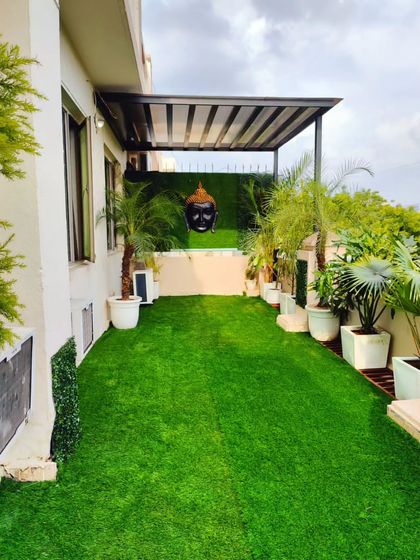 A peaceful terrace garden design. This space features a lush artificial lawn, a pergola for shade, and a Buddha head feature wall for a touch of serenity.
