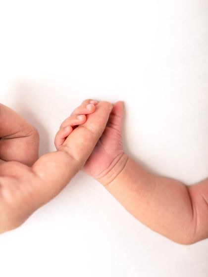 A newborn baby's hand gently holds onto their parent's finger. This is a classic newborn detail shot that symbolizes trust and love.