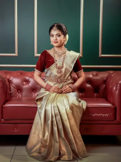 This image captures the bride seated on a red sofa against a dark green paneled wall, a classic combination that exudes luxury. The pose is graceful and showcases the full saree.