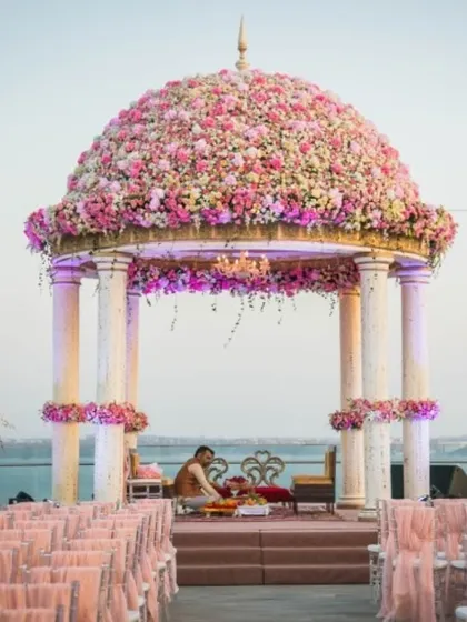 A magnificent dome-shaped mandap covered entirely in pink flowers, set by the sea. This is the epitome of a luxurious destination wedding, blending architectural structure with natural beauty.