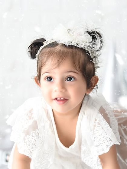 A close-up portrait from a winter-themed first birthday shoot. The falling snow effect adds a touch of wonder to her sweet expression.