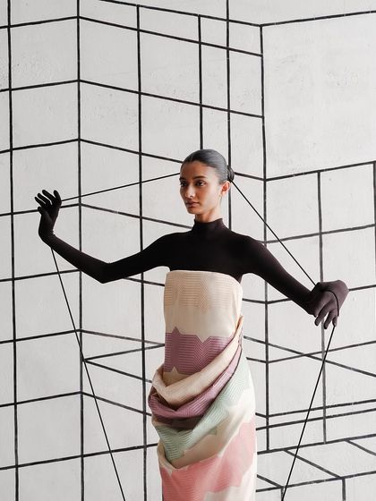 A model holds threads that seem to emerge from the grid behind her, physically connecting her to the architectural space.
