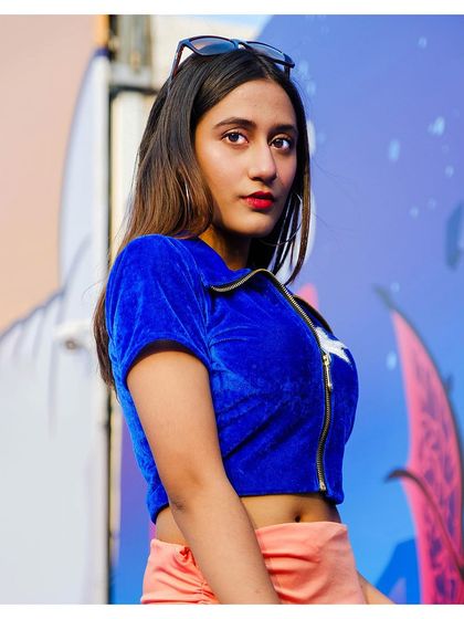 A close-up portrait of a cosplayer as Nico Robin from One Piece. We focus on capturing striking expressions and details, like the vibrant blue top and confident look, set against a colorful event mural.