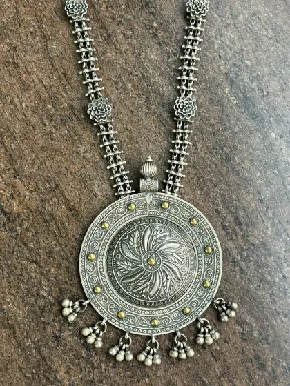 A unique and antique oxidised silver pendant. This large, circular piece has a beautiful floral-inspired carving and is accented with small gold-tone dots and dangling silver beads.