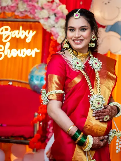 The radiant mom-to-be at her baby shower. She is glowing in a beautiful red and gold saree, adorned with traditional floral jewelry.