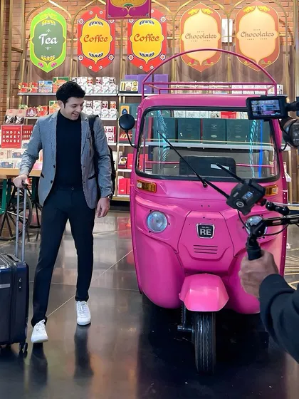 Posing next to a quirky pink auto-rickshaw inside the airport for a fun scene. I'm always ready to engage with the props and environment to create a memorable shot.