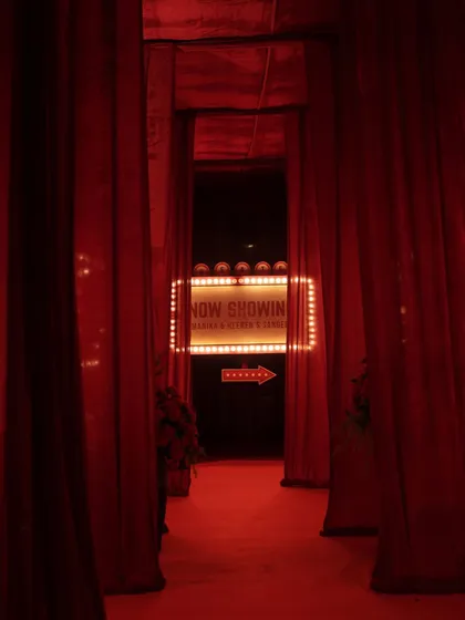 The dramatic entrance walkway for the Sangeet, lined with heavy red velvet curtains, leading guests towards the glowing marquee sign.