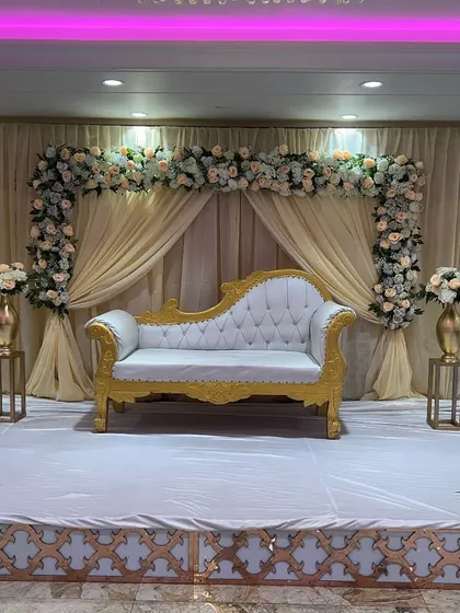 A classic and sophisticated stage design with a cream and gold color palette, featuring a floral arch, elegant drapes, and a royal diwan.