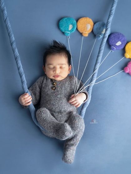 A creative newborn portrait where the baby appears to be floating away with a bunch of colorful felt balloons. This simple yet imaginative setup is done against a solid blue background.