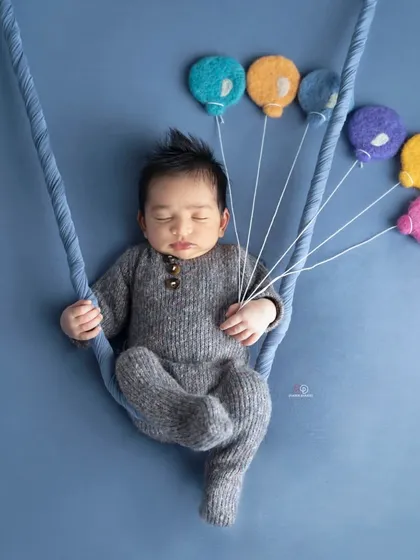 A creative newborn portrait where the baby appears to be floating away with a bunch of colorful felt balloons. This simple yet imaginative setup is done against a solid blue background.