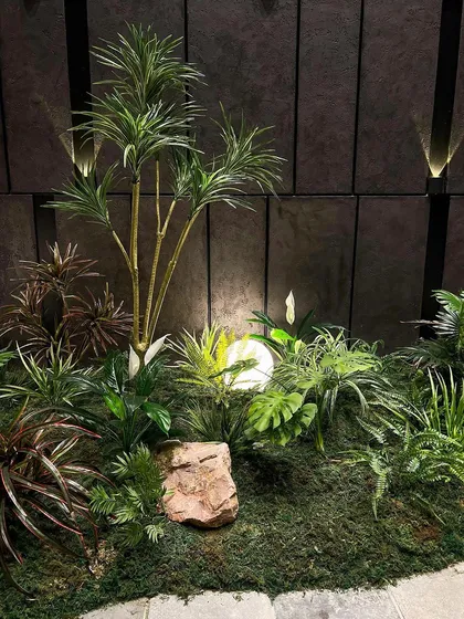 A detailed shot of a section of our indoor garden, showcasing a mix of faux tropical plants like palms and peace lilies. The arrangement is designed to look natural and untamed, like a slice of a real forest floor.