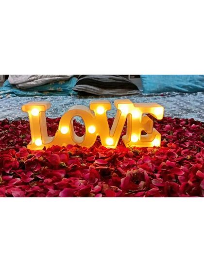 A close-up of a classic romantic detail for a "Just Married" room. A large heart made of red rose petals with a lit-up "LOVE" marquee sign placed in the center on the bed.