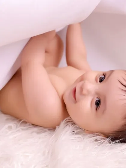 A peek-a-boo moment! This baby is playing under a white sheet on a fluffy rug, a simple and candid shot that captures pure childhood joy.
