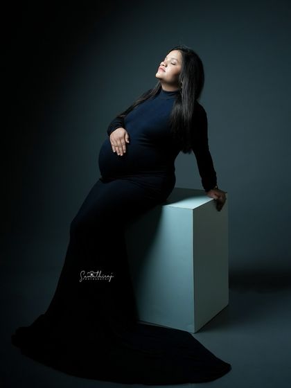 A dramatic and artistic portrait of a mother-to-be seated on a block. The strong lighting and shadows create a powerful silhouette that emphasizes her strength and beauty.