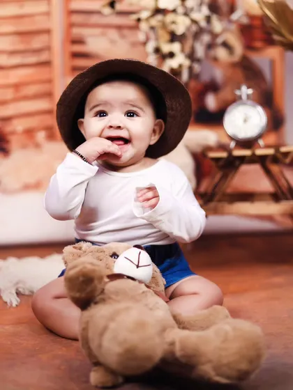 A candid moment of a baby boy playing with his teddy bear during a rustic-themed studio session.