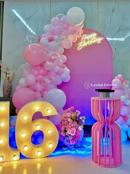 A sweet sixteen celebration with a vibrant pink theme, featuring a large balloon arch and light-up marquee numbers.