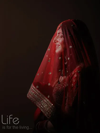 A dramatic, low-key portrait of a bride, with light catching her smile and the delicate texture of her red veil.