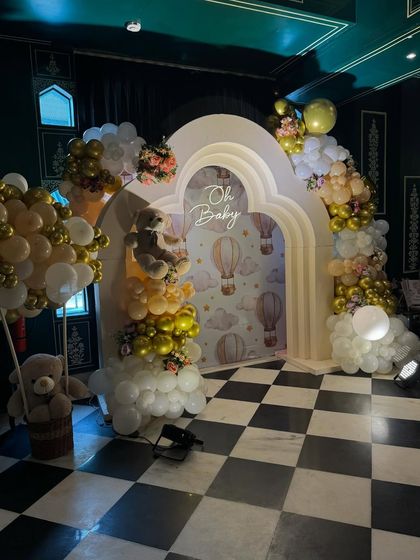 The full view of the 'Oh Baby' photo booth, featuring double arches, a hot air balloon backdrop, and teddy bears floating in balloon baskets.